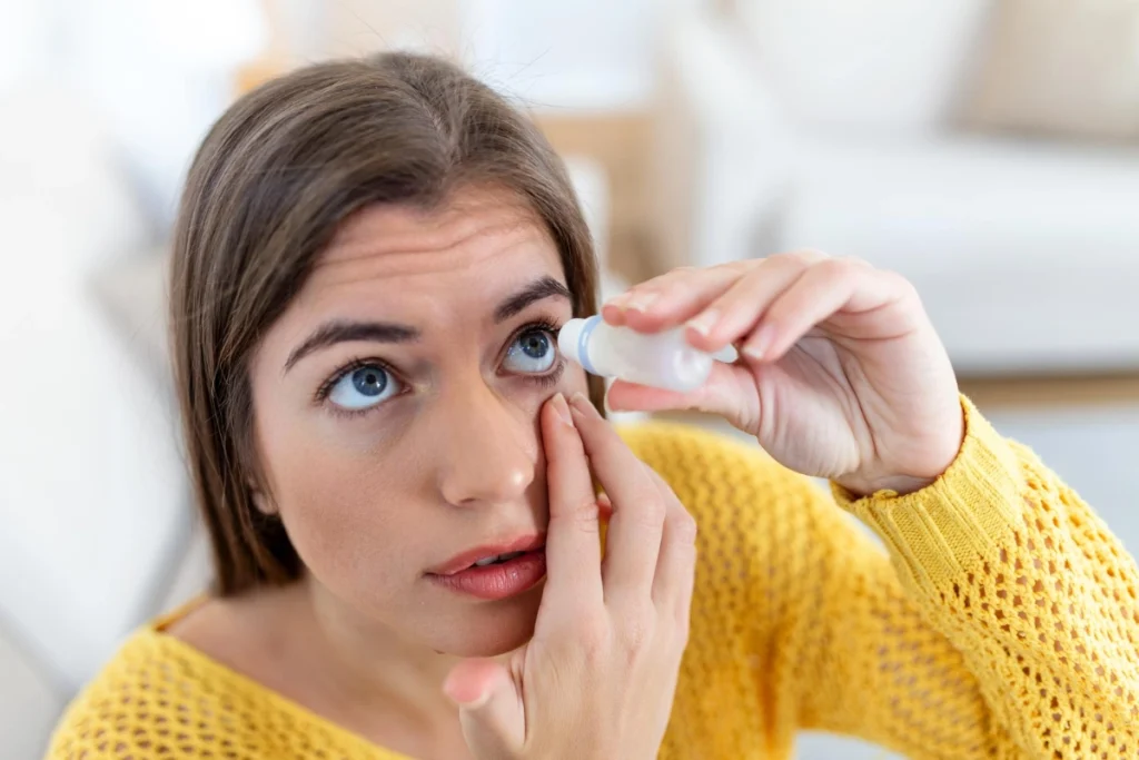 A woman in a yellow jumper using eye drops